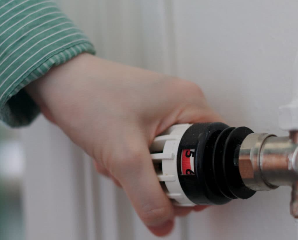 Bilden visar en hand som justerar en termostatventil på ett element.