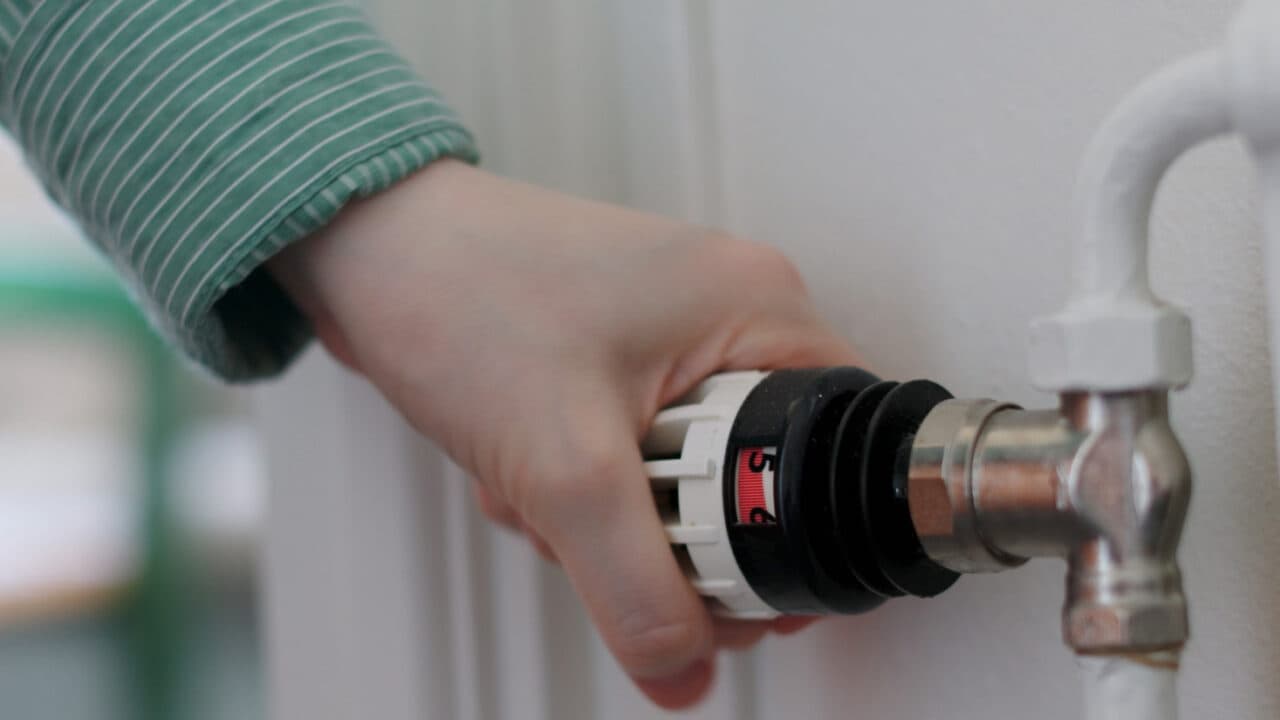 Bilden visar en hand som justerar en termostatventil på ett element.