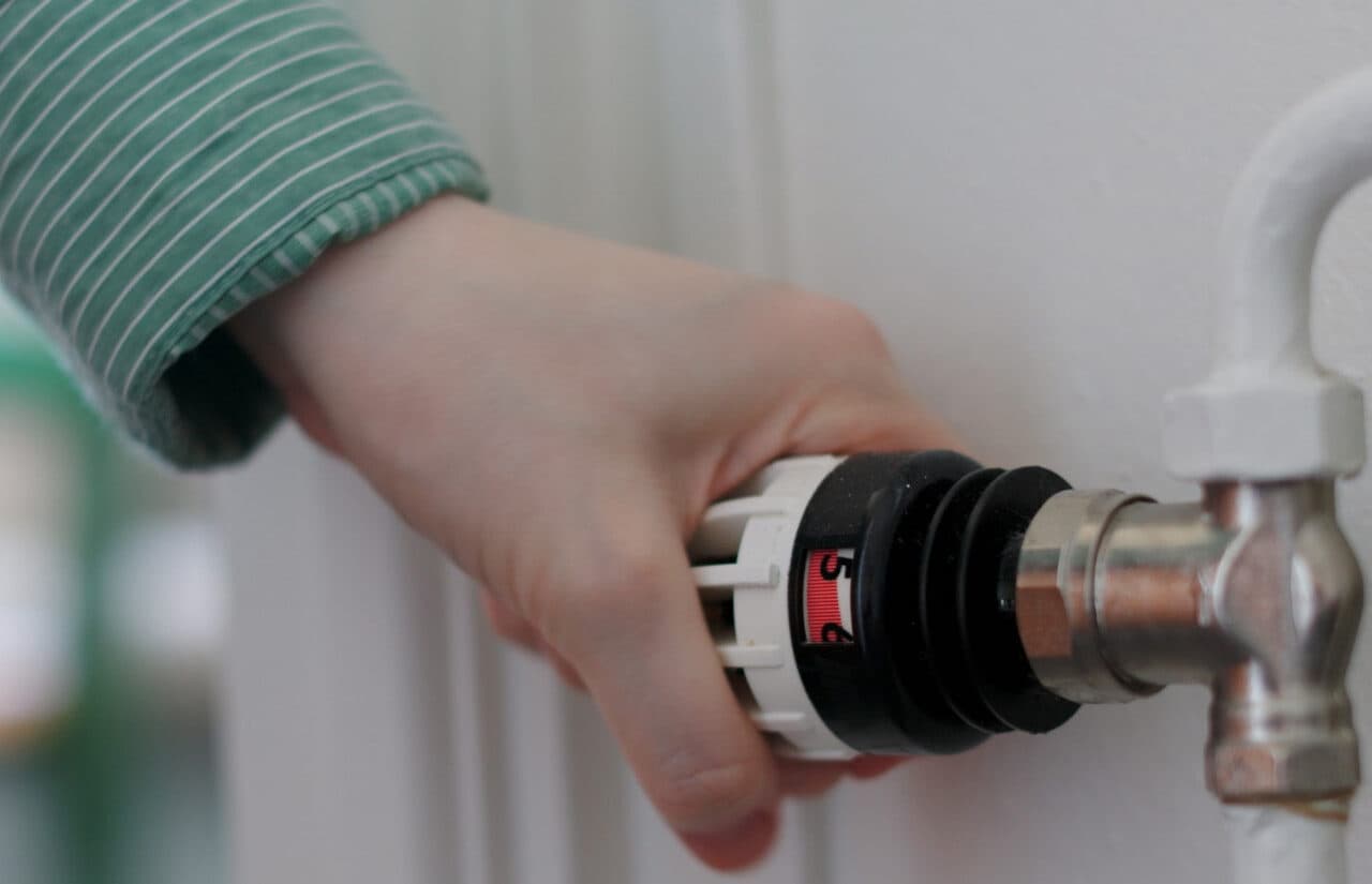 Bilden visar en hand som justerar en termostatventil på ett element.