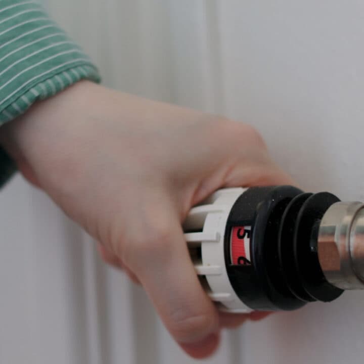 Bilden visar en hand som justerar en termostatventil på ett element.
