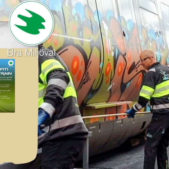 Bilden visar två personer som arbetar med att ta bort graffiti från ett tåg. De använder en produkt som marknadsförs som miljövänlig, vilket framgår av texten &#34;Bra Miljöval&#34; och etiketten på produkten. Tåget är täckt med färgglad graffiti.