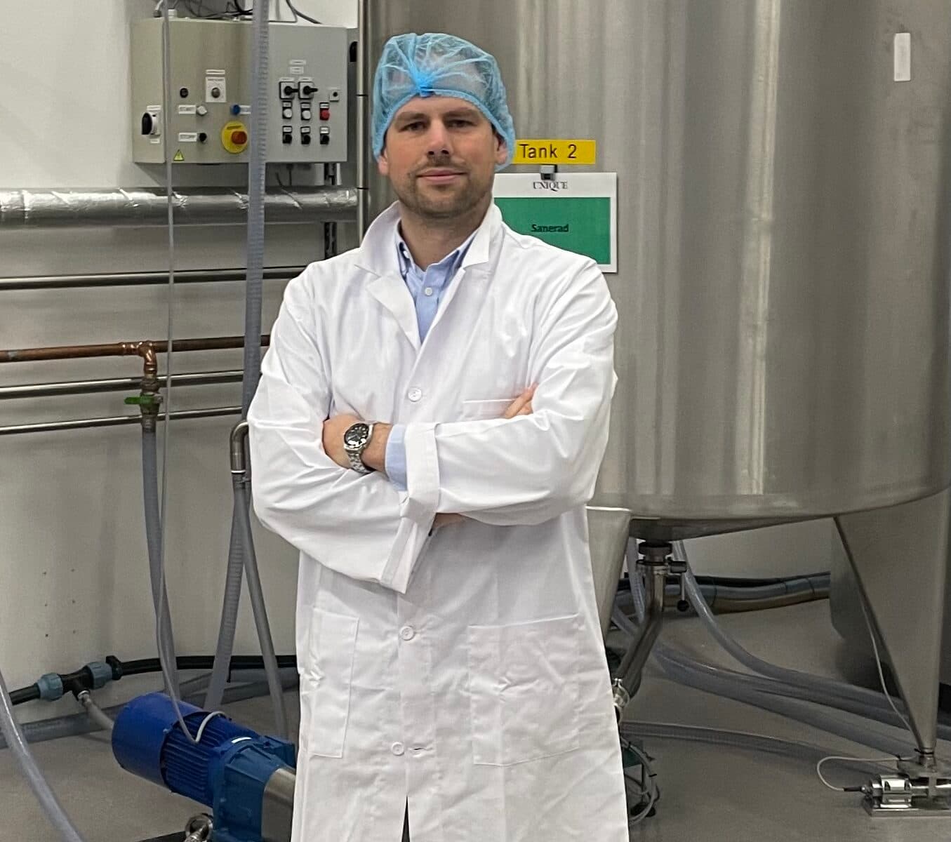 Bilden visar en person i en laboratoriemiljö. Personen bär en vit labbrock, blå skoskydd och en blå ...