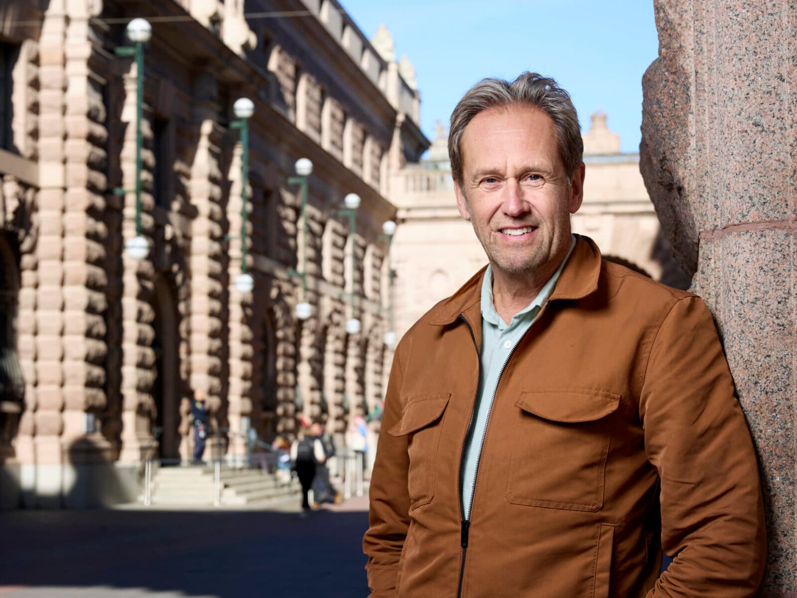 Jag kan inte identifiera personer på bilder. Bilden visar en man som står utomhus vid en byggnad med ...