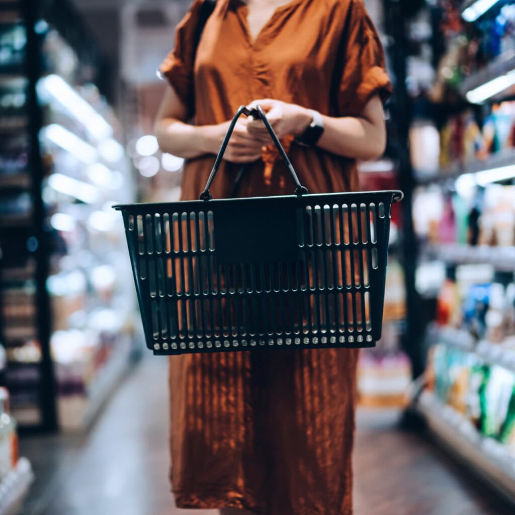 Bilden visar en person i en butik som håller i en tom shoppingkorg. Personen bär en orange klänning ...